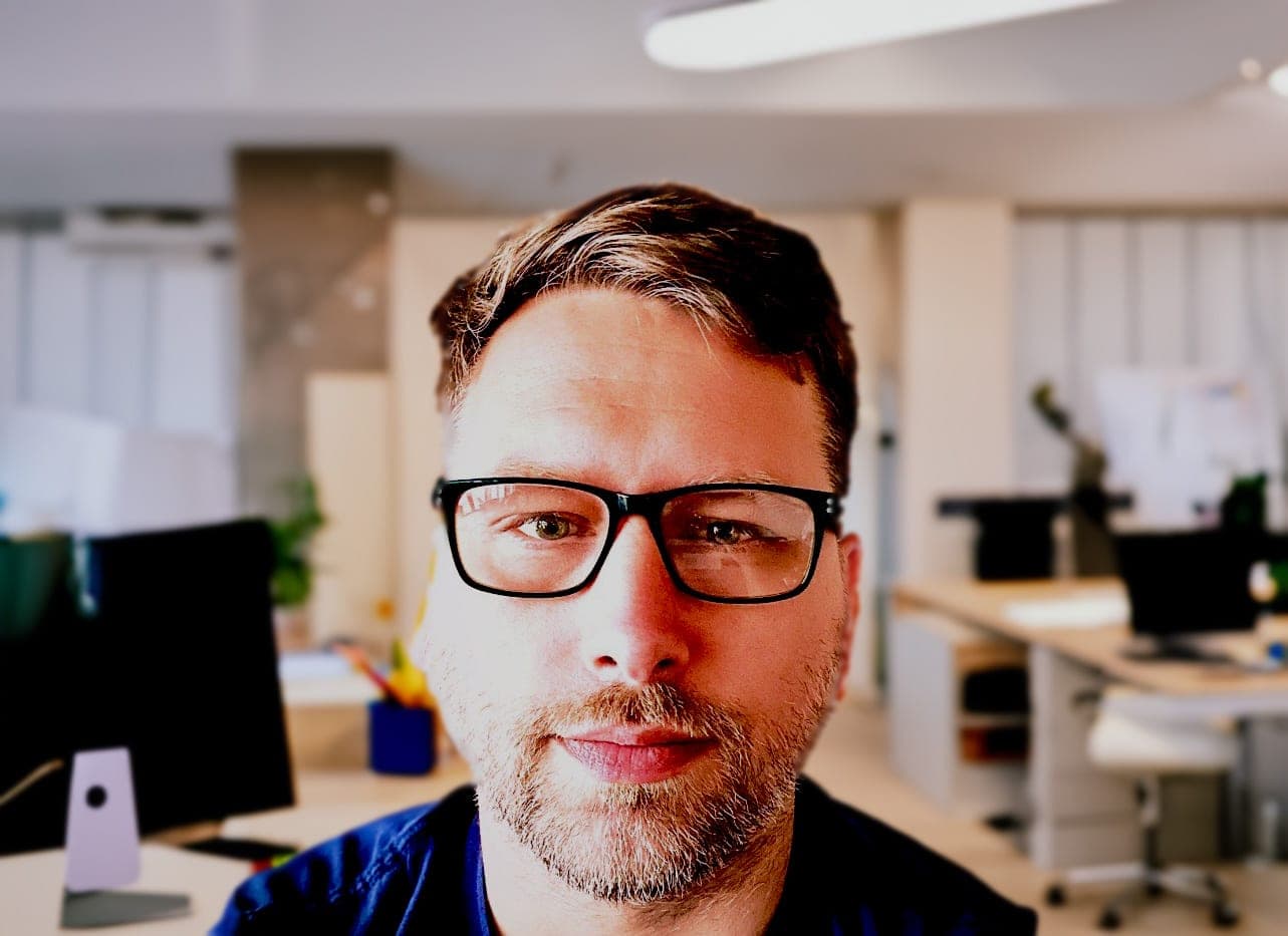 Simon Bromfield, in glasses and a navy shirt, at his desk in an office.