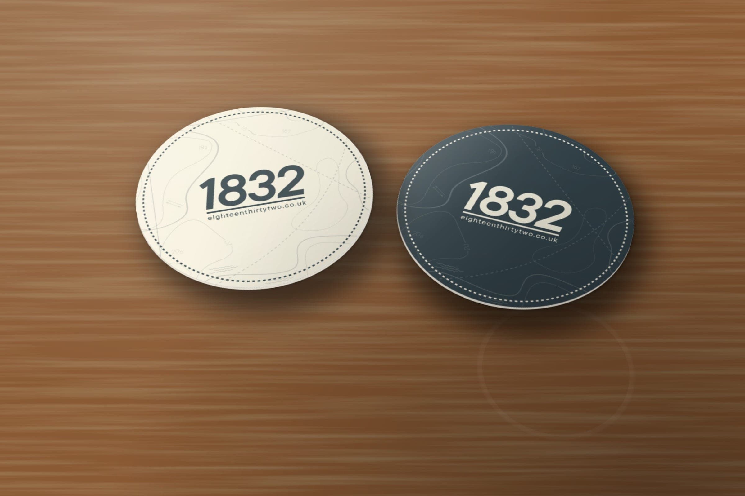 Mockup: 1832 round beermats, the logo on cream chart contours on one and cream on slate on the other.